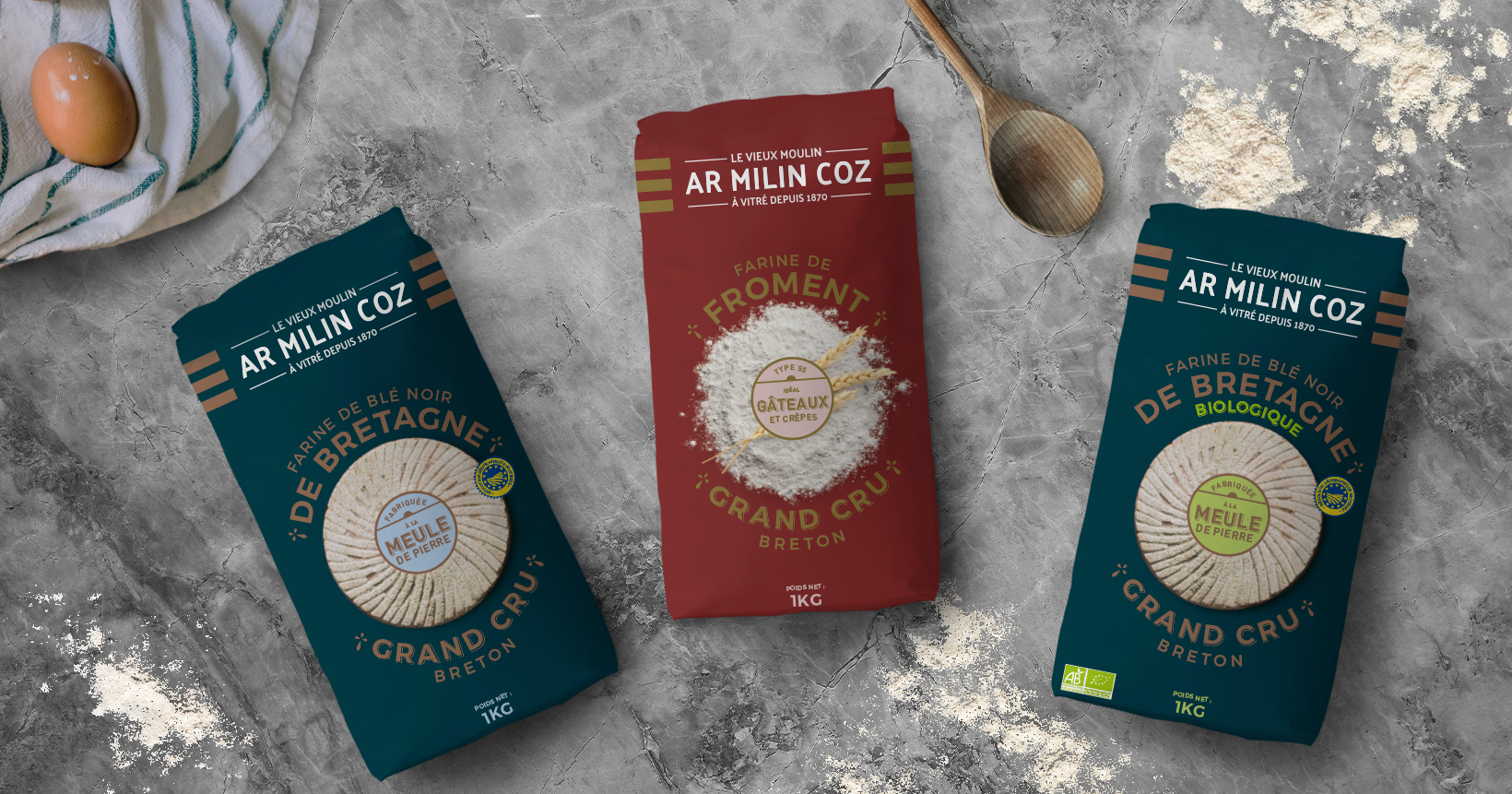 Gamme de trois packagings Ar Milin Coz, vue de dessus, sur un plan de travail avec des ustensiles et de la farine étalée