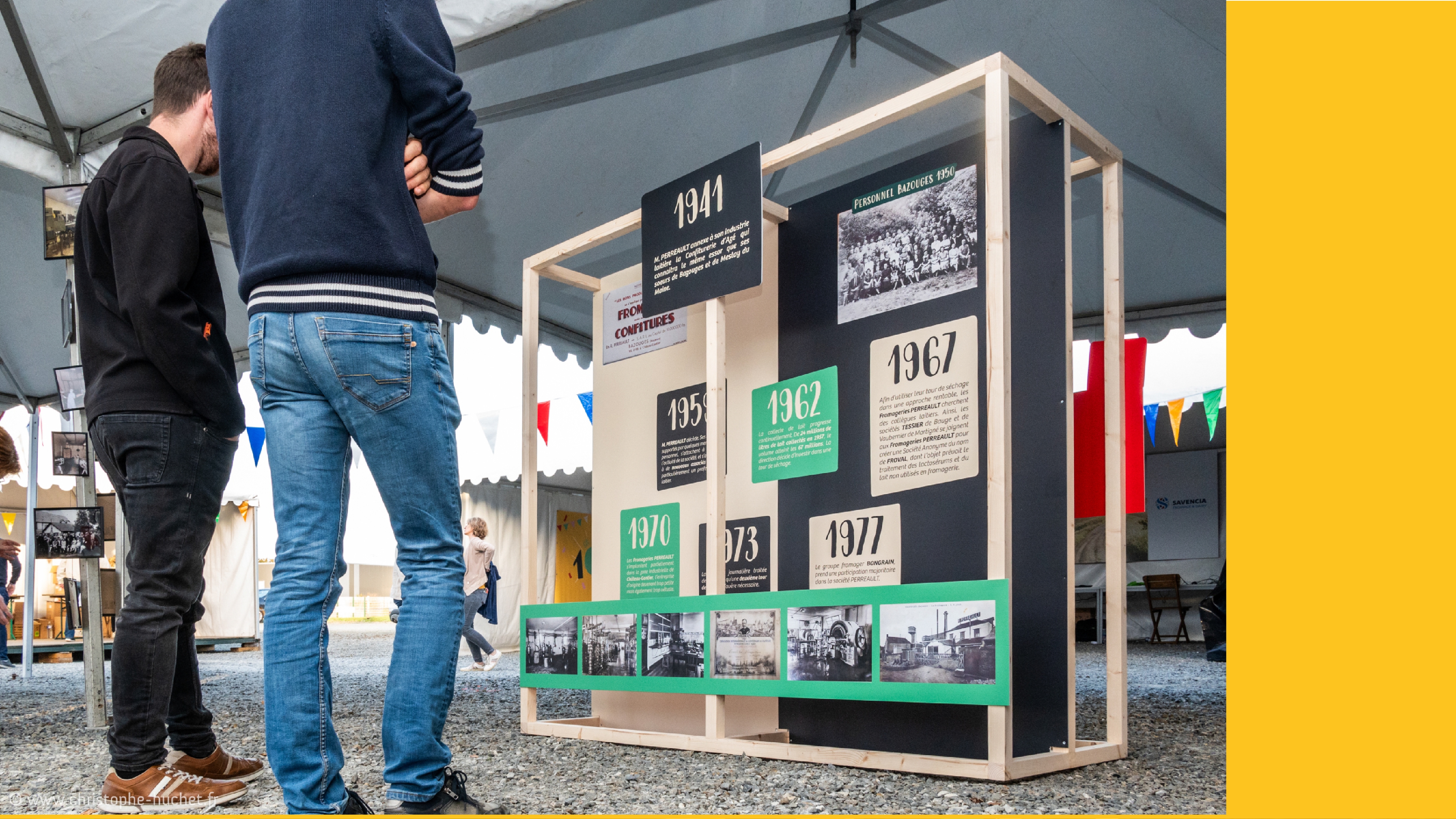 Un panneau installé lors de l’évènement avec des informations historique sur les Fromageries Perreault devant lequel se tiennent 2 personnes